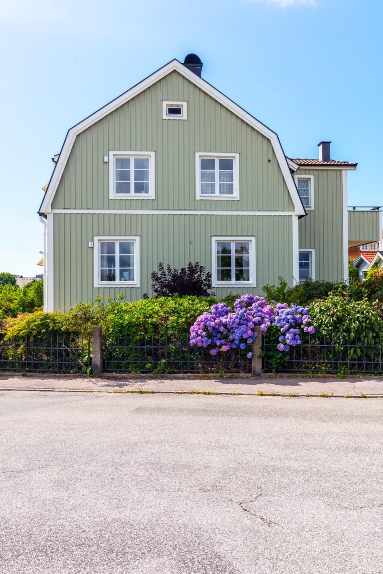 Ett trähus med en fräsch grön färg och vita detaljer, omgivet av en trädgård med blomstrande lila hortensior