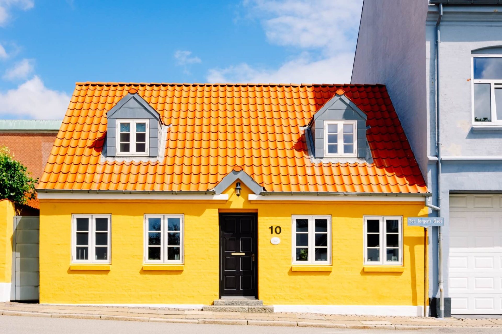 I en stadsmiljö hittar vi ett hus som utmärker sig med sitt gula skal, orange tak och svarta ingångar